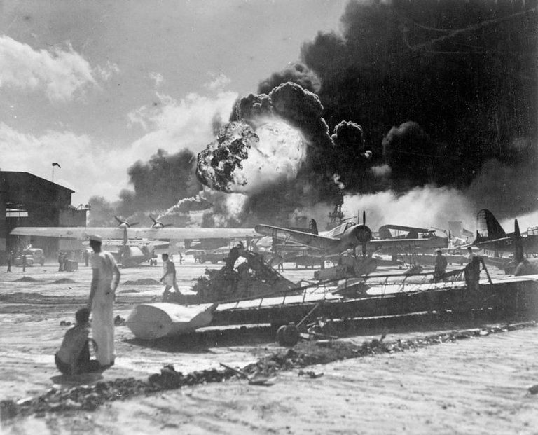 American sailors stand amid wrecked planes at the Ford Island seaplane base, watching as the USS Shaw explodes in the center background during the Japanese raid on Pearl Harbor, Hawaii on December 7, 1941..jpg