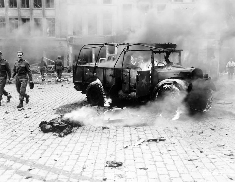 Bystanders look on as a boy's burning corpse lies next to the jeep he was in, which was struck by a German V-2 rocket in Antwerp, Belgium on November 27, 1944..jpg