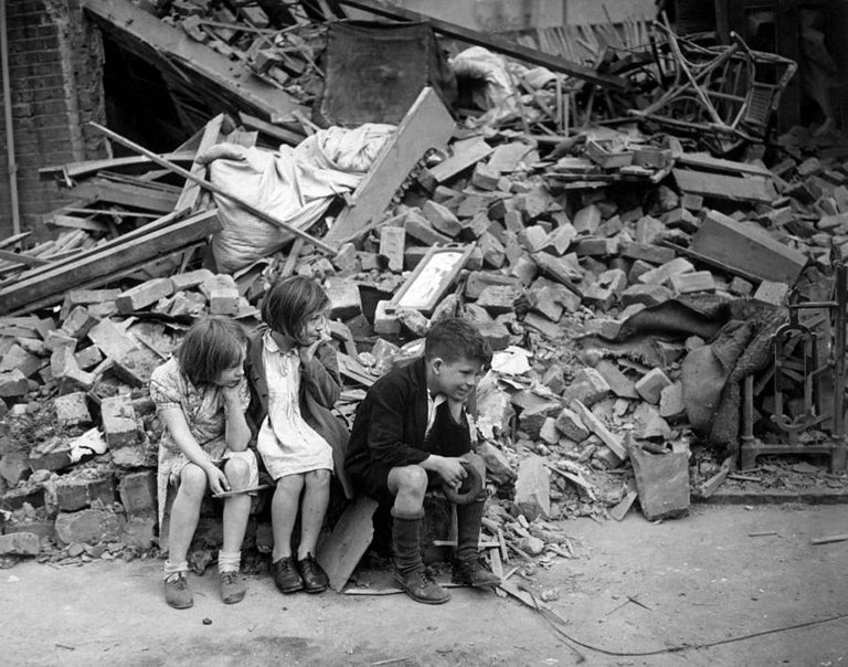 Children of an eastern suburb of London, who have been made homeless by German bombings, sit outside the wreckage of what was their home, September 1940..jpg